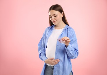 Photo of Expecting twins. Pregnant woman holding two pacifiers on pink background