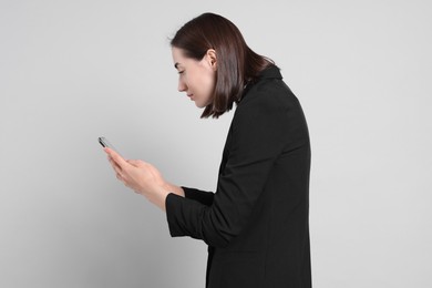 Woman with poor posture using smartphone on gray background