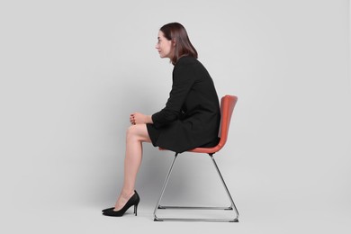 Woman with poor posture sitting on chair against gray background