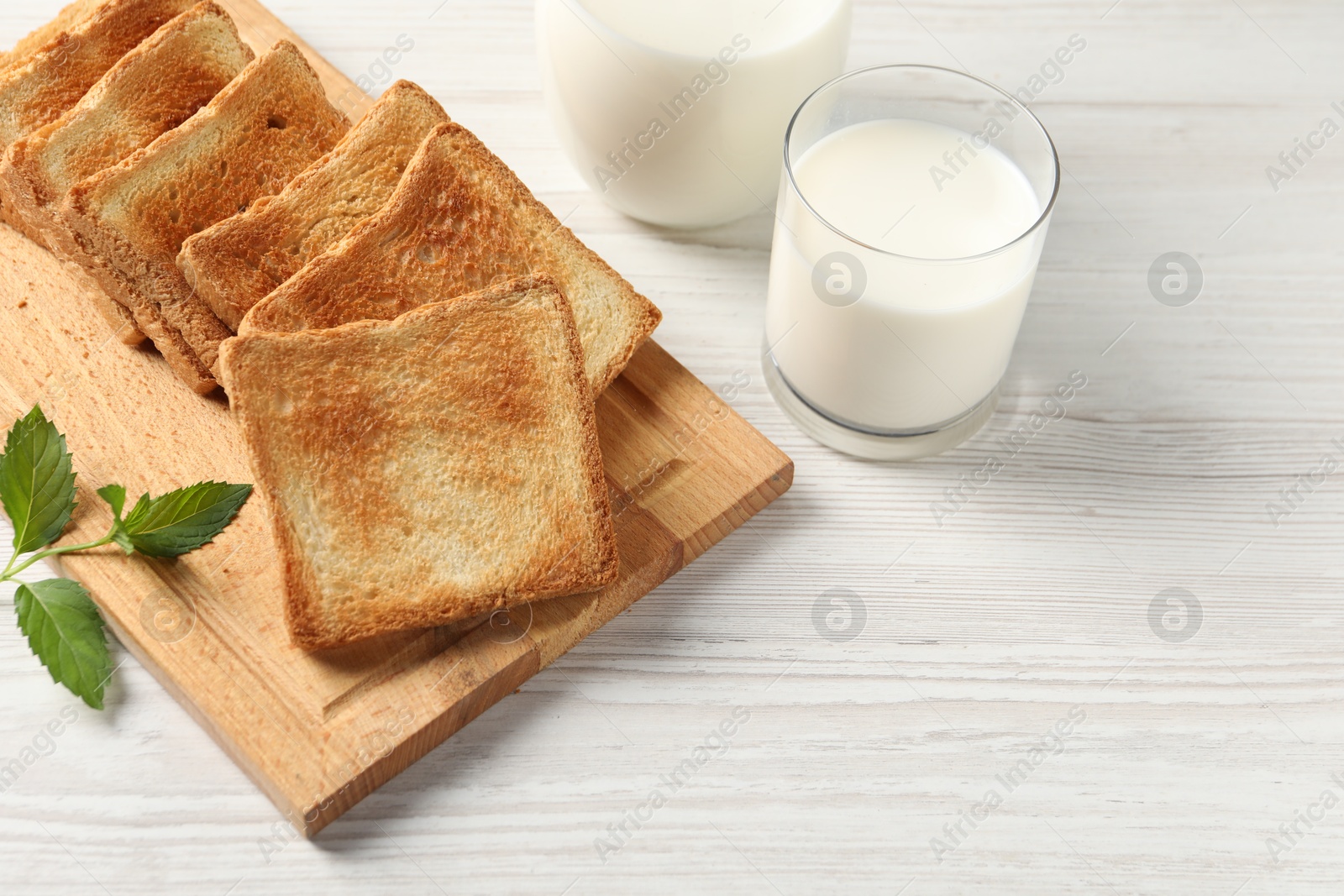 Photo of Delicious toasts with milk on white wooden table