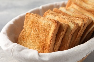 Photo of Delicious toasts in basket on light table, closeup