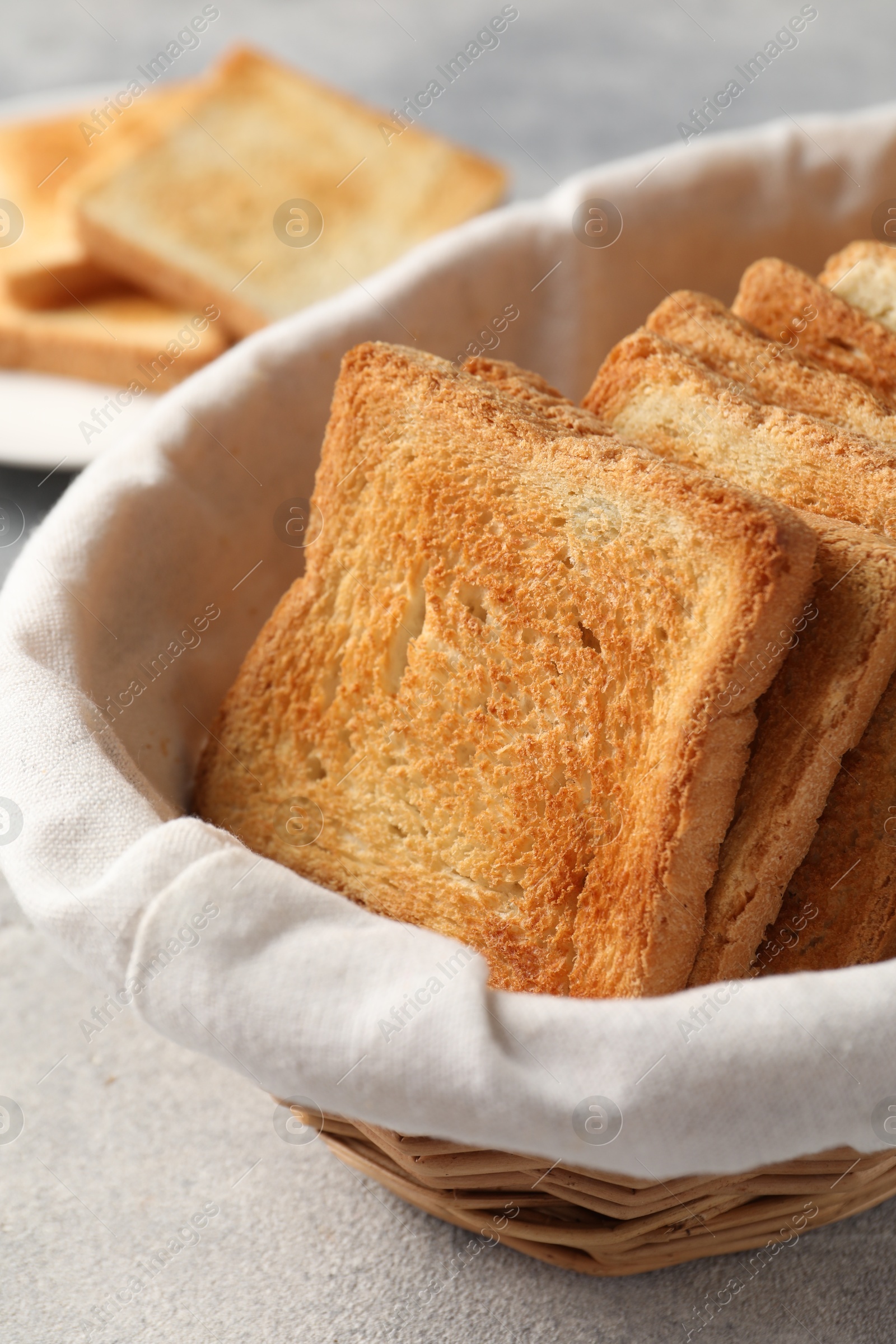 Photo of Delicious toasts in basket on light table, closeup