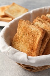 Photo of Delicious toasts in basket on light table, closeup