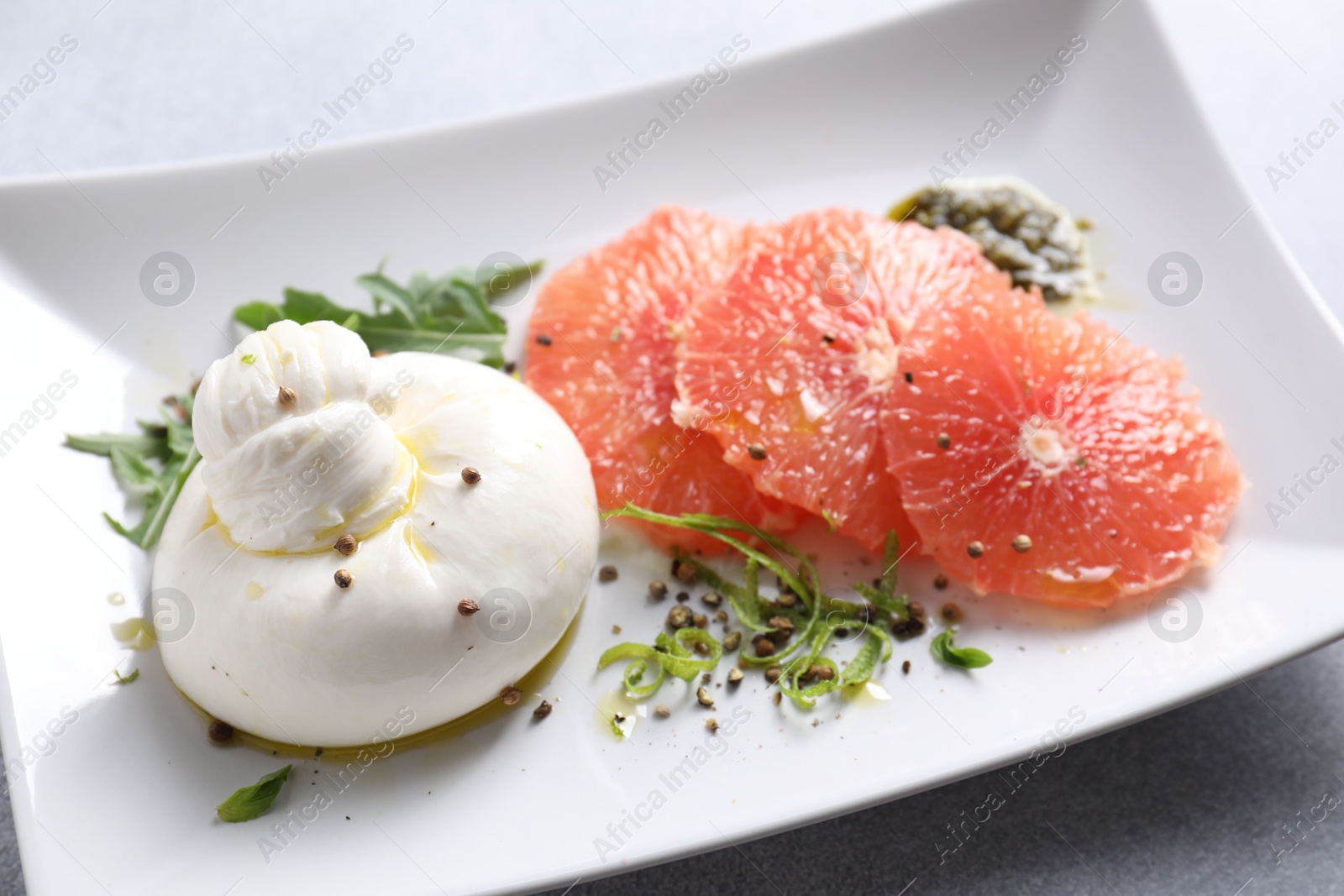 Photo of Delicious burrata cheese, grapefruit and spices on light grey table, closeup