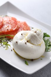 Photo of Delicious burrata cheese, grapefruit and spices on light grey table, closeup