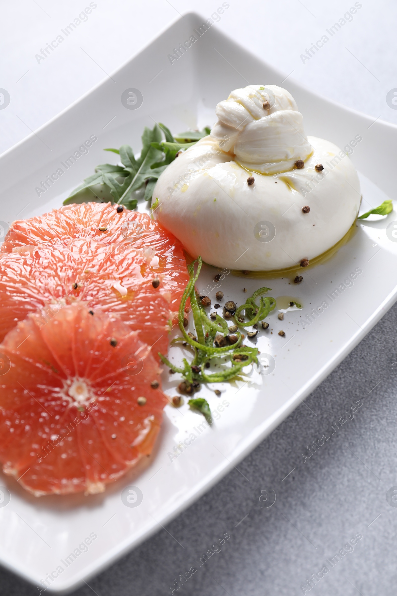 Photo of Delicious burrata cheese, grapefruit and spices on light grey table, closeup