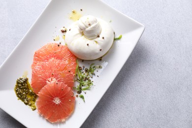 Photo of Delicious burrata cheese, grapefruit and spices on light grey table, top view. Space for text