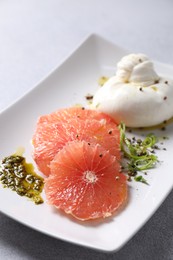 Photo of Delicious burrata cheese, grapefruit and spices on light grey table, closeup