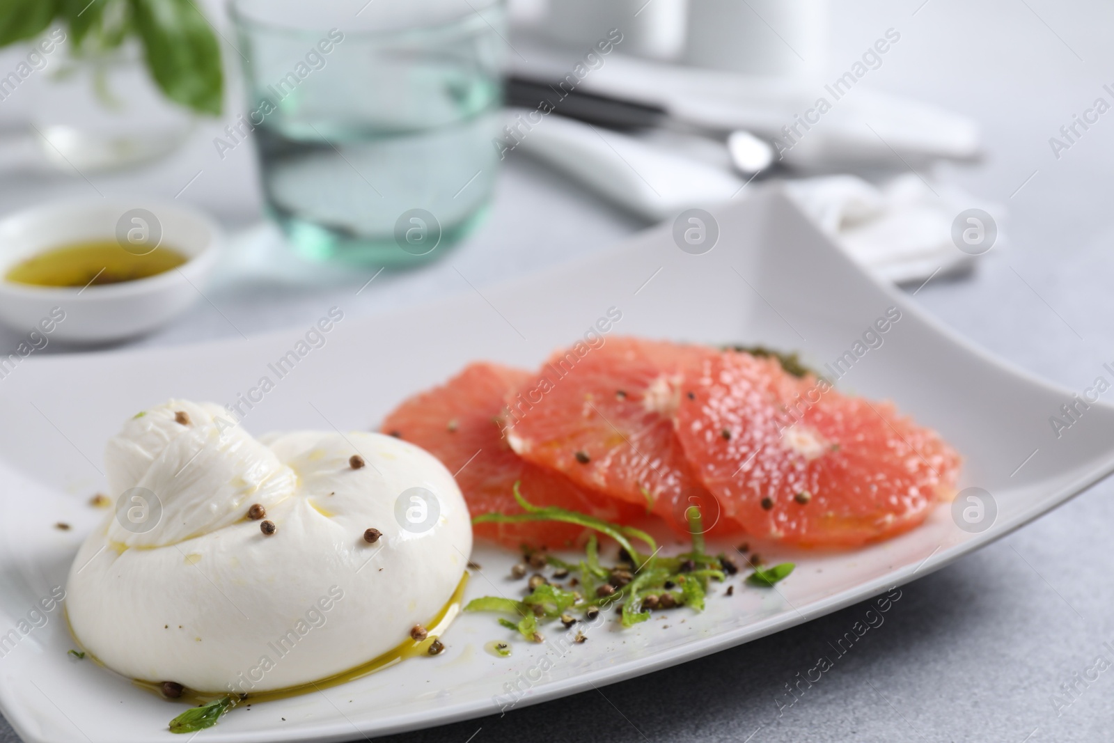 Photo of Delicious burrata cheese, grapefruit and spices on light grey table, closeup