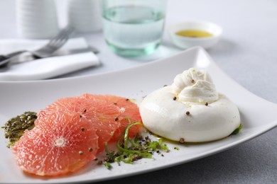 Photo of Delicious burrata cheese, grapefruit and spices on light grey table, closeup