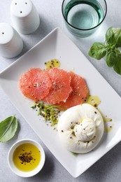 Photo of Delicious burrata cheese and grapefruit served on light grey table, top view