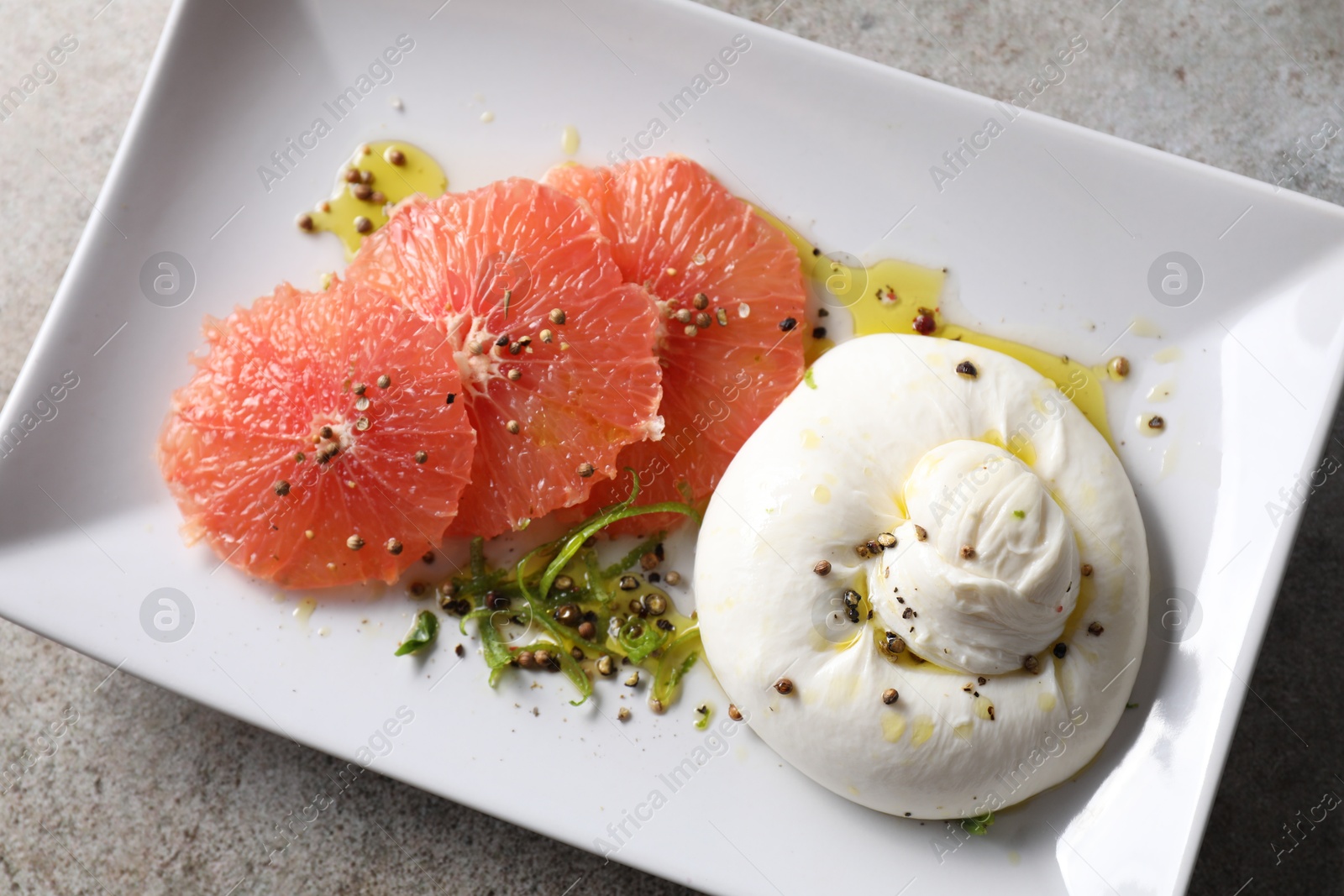 Photo of Delicious burrata cheese, grapefruit and spices on grey table, top view