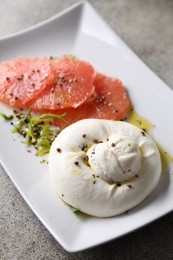 Photo of Delicious burrata cheese, grapefruit and spices on grey table, closeup