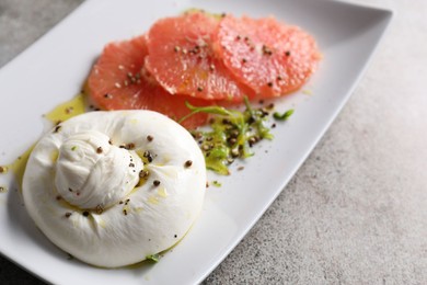 Delicious burrata cheese, grapefruit and spices on grey table, closeup