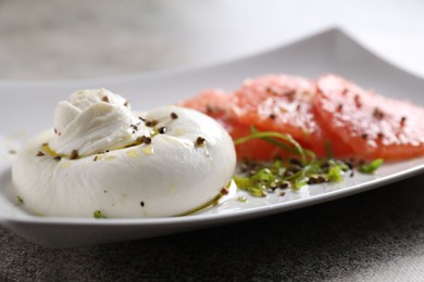 Photo of Delicious burrata cheese, grapefruit and spices on grey table, closeup