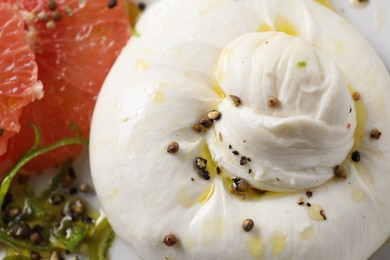 Photo of Delicious burrata cheese, grapefruit and spices on plate, closeup