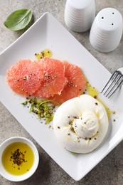 Photo of Delicious burrata cheese, grapefruit and spices on grey table, top view