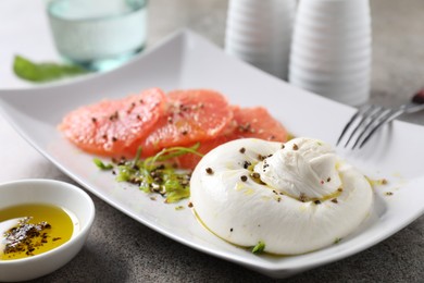 Photo of Delicious burrata cheese, grapefruit and spices on grey table, closeup