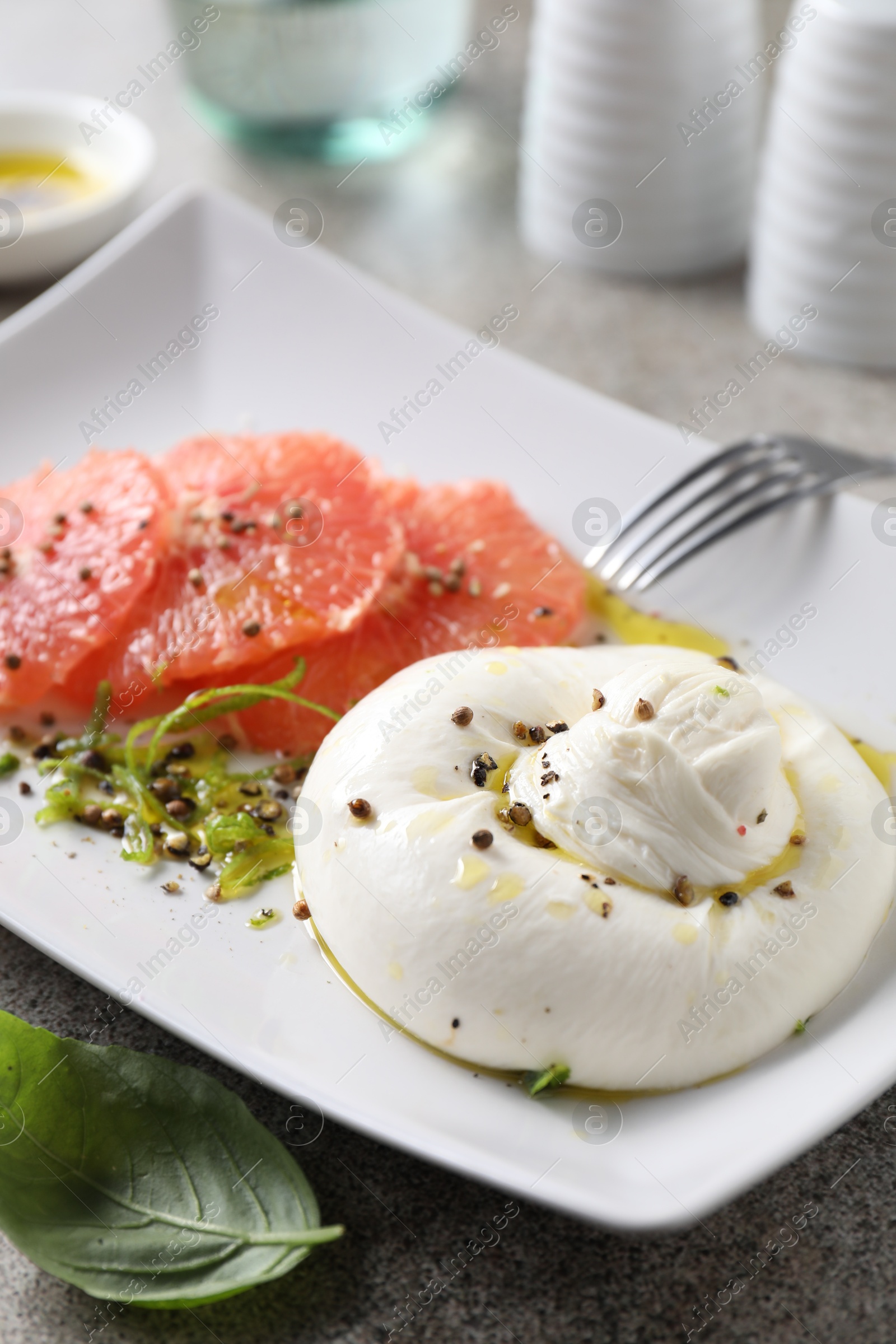 Photo of Delicious burrata cheese, grapefruit and spices on grey table, closeup