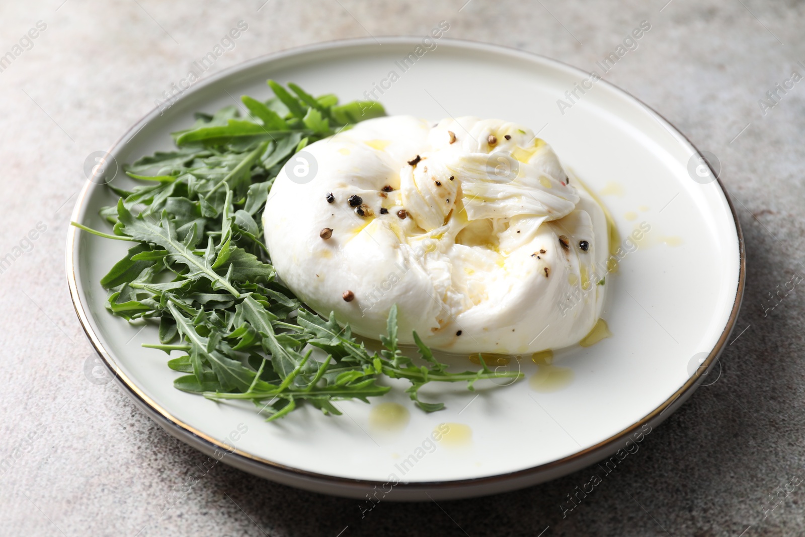 Photo of Delicious burrata cheese, arugula and spices on grey table, closeup