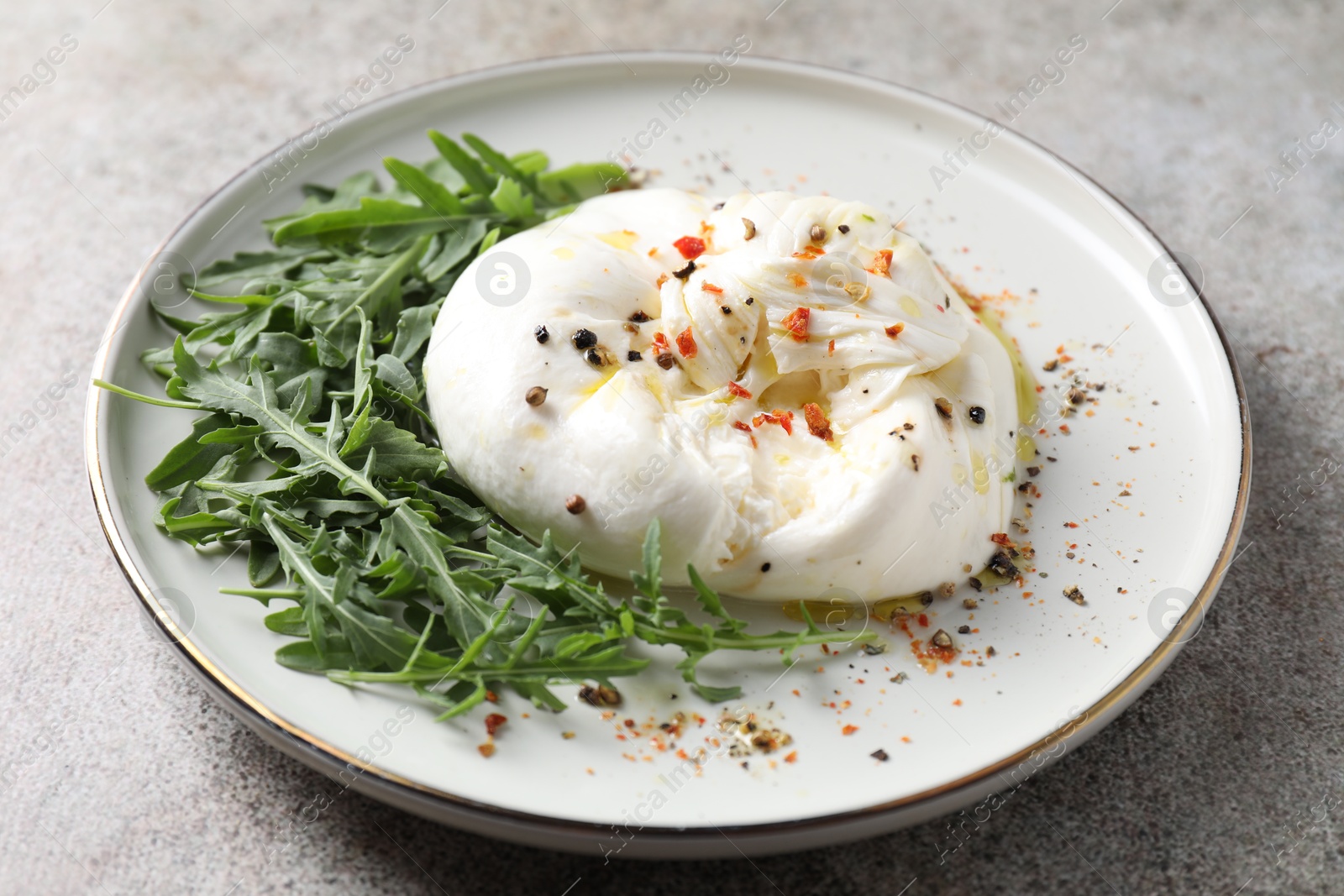 Photo of Delicious burrata cheese, arugula and spices on grey table, closeup