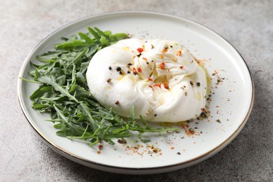 Photo of Delicious burrata cheese, arugula and spices on grey table, closeup