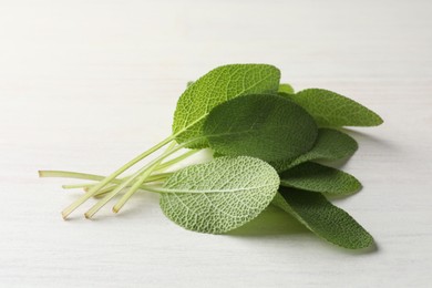 Photo of Fresh sage leaves on light wooden table, closeup