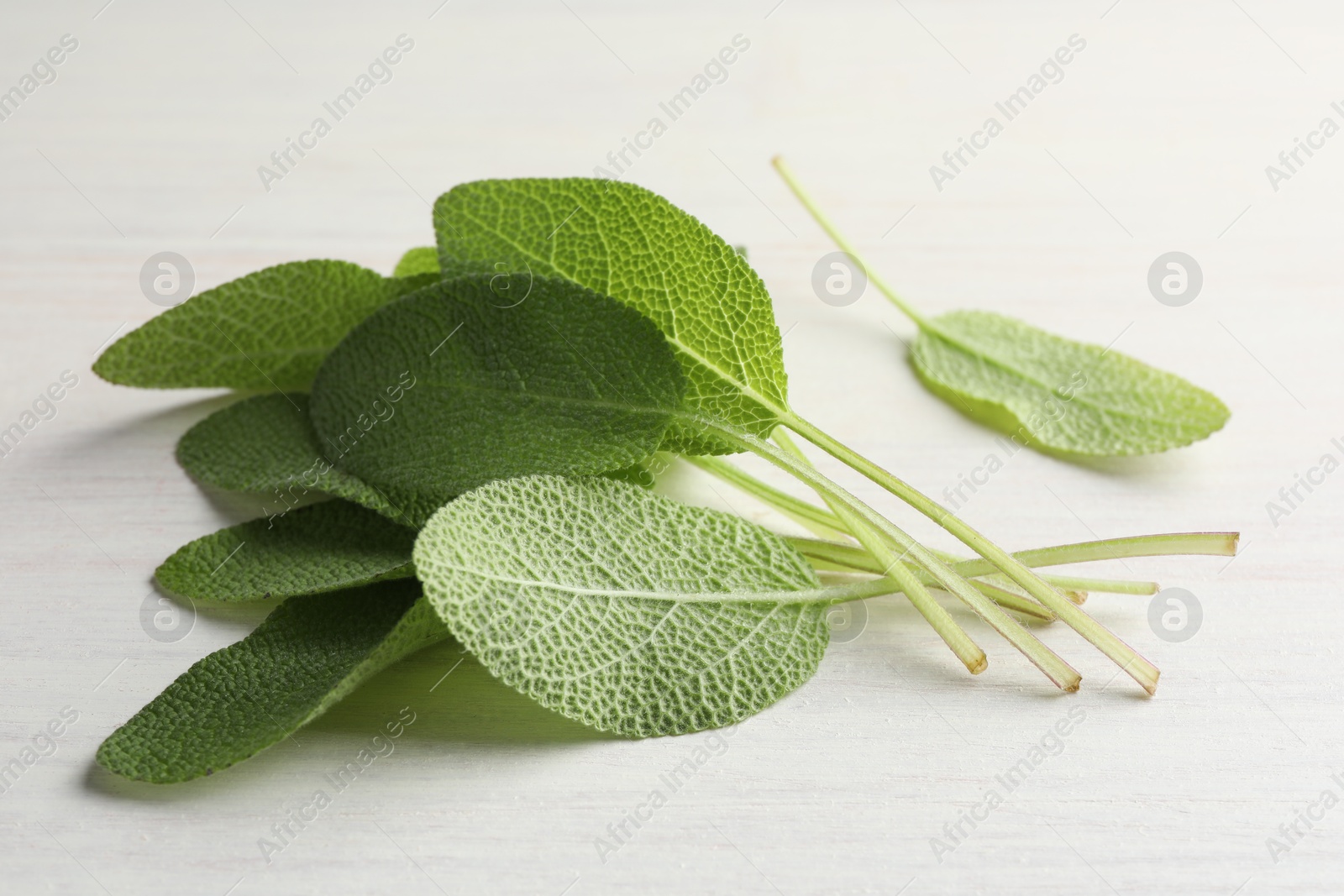 Photo of Fresh sage leaves on light wooden table, closeup