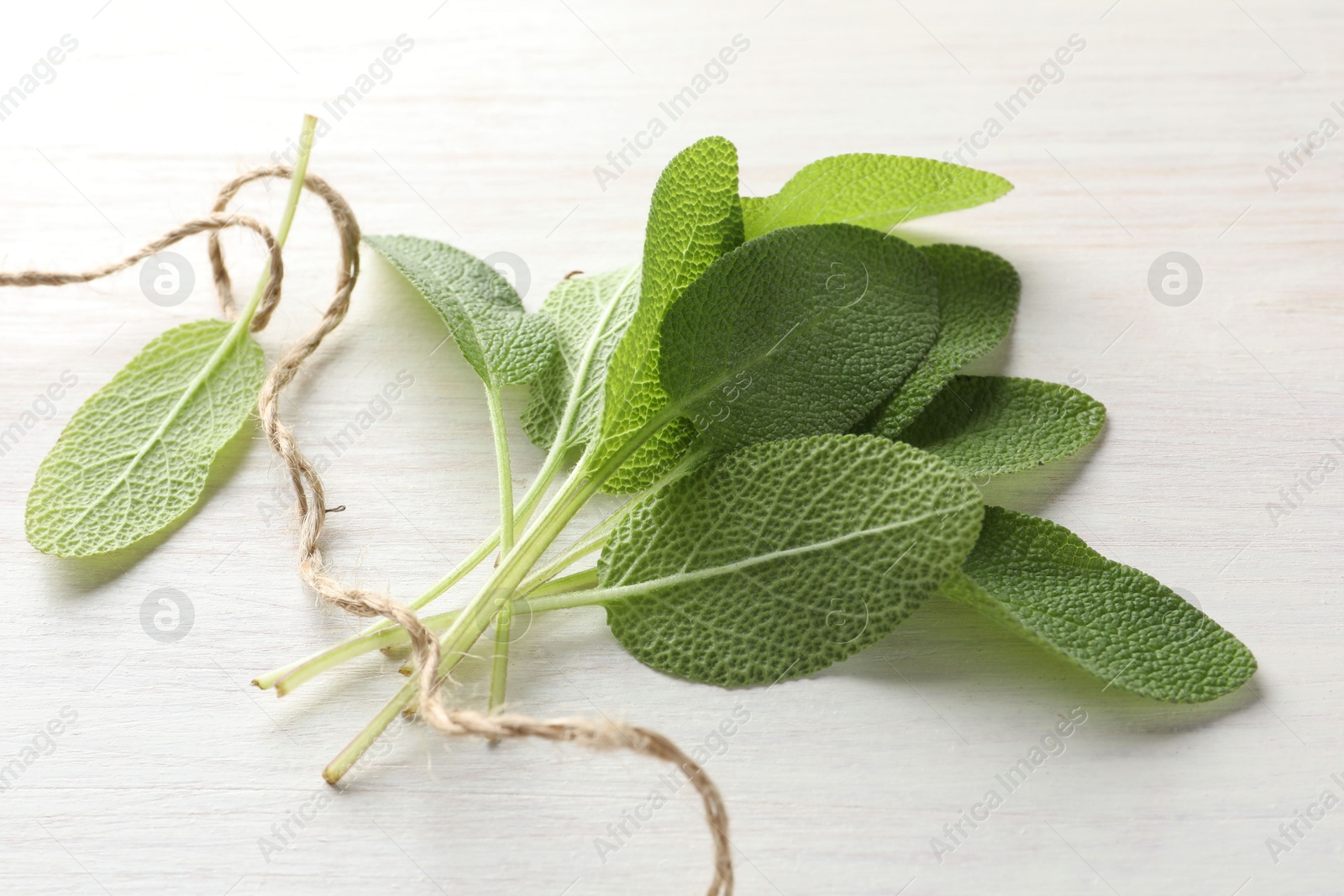 Photo of Fresh sage leaves and thread on light wooden table, top view