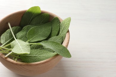 Photo of Fresh sage leaves in bowl on light wooden table, closeup. Space for text