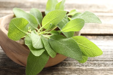 Photo of Fresh sage leaves in bowl on wooden table, closeup