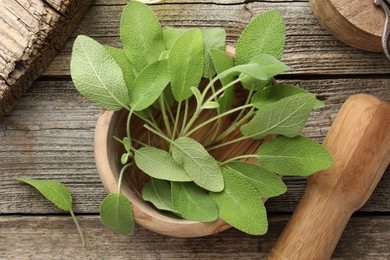 Photo of Fresh sage leaves, mortar and pestle on wooden table, flat lay