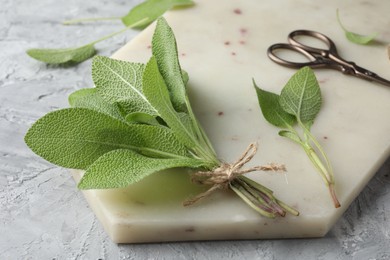 Photo of Bunch of fresh sage leaves and scissors on gray textured table, closeup