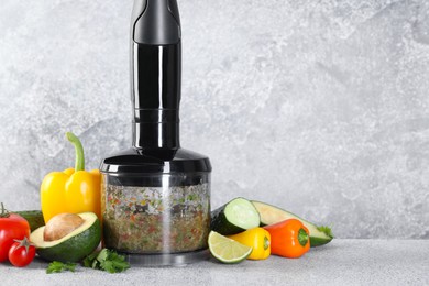 Photo of Hand blender with mixture of ingredients and fresh products on light grey table. Space for text