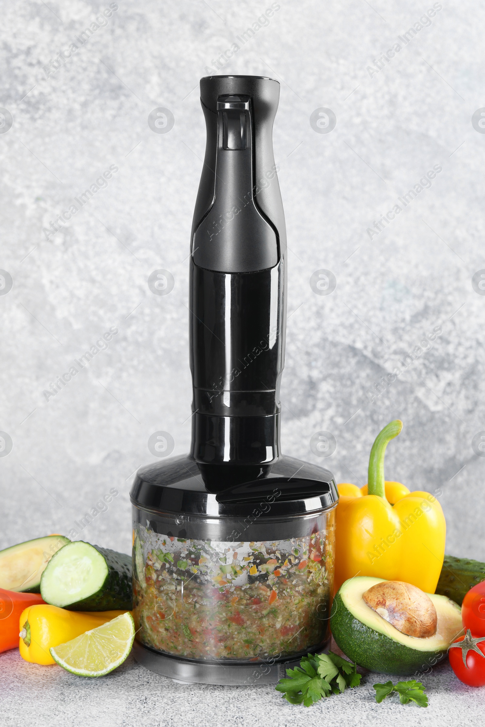 Photo of Hand blender with mixture of ingredients and fresh products on light grey table