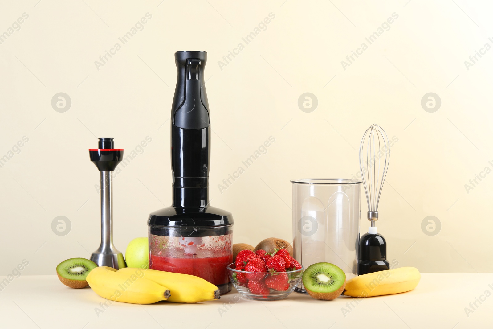 Photo of Hand blender kit, mixture of ingredients and fresh fruits on beige background