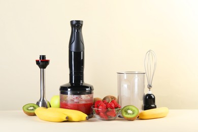 Photo of Hand blender kit, mixture of ingredients and fresh fruits on beige background