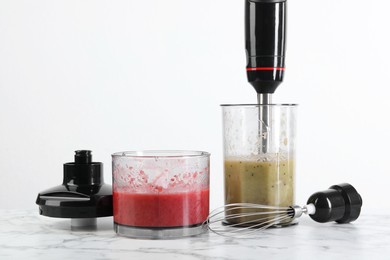 Photo of Hand blender kit and mixtures of ingredients on white marble table