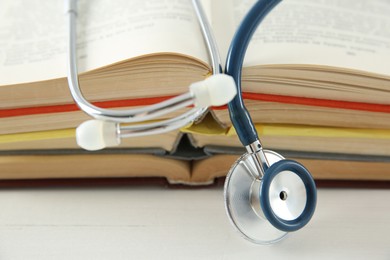 One new medical stethoscope and books on white wooden table, closeup