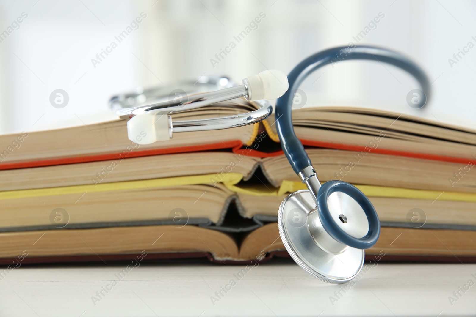 Photo of One new medical stethoscope and books on white wooden table, closeup