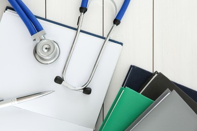 One new medical stethoscope and books on white wooden table, flat lay