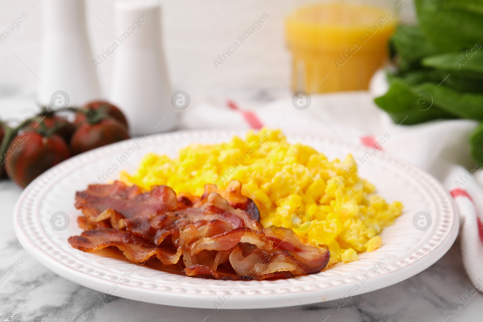 Photo of Delicious scrambled eggs with bacon in plate on white marble table, closeup