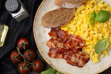 Photo of Delicious scrambled eggs with bacon and products on wooden table, flat lay