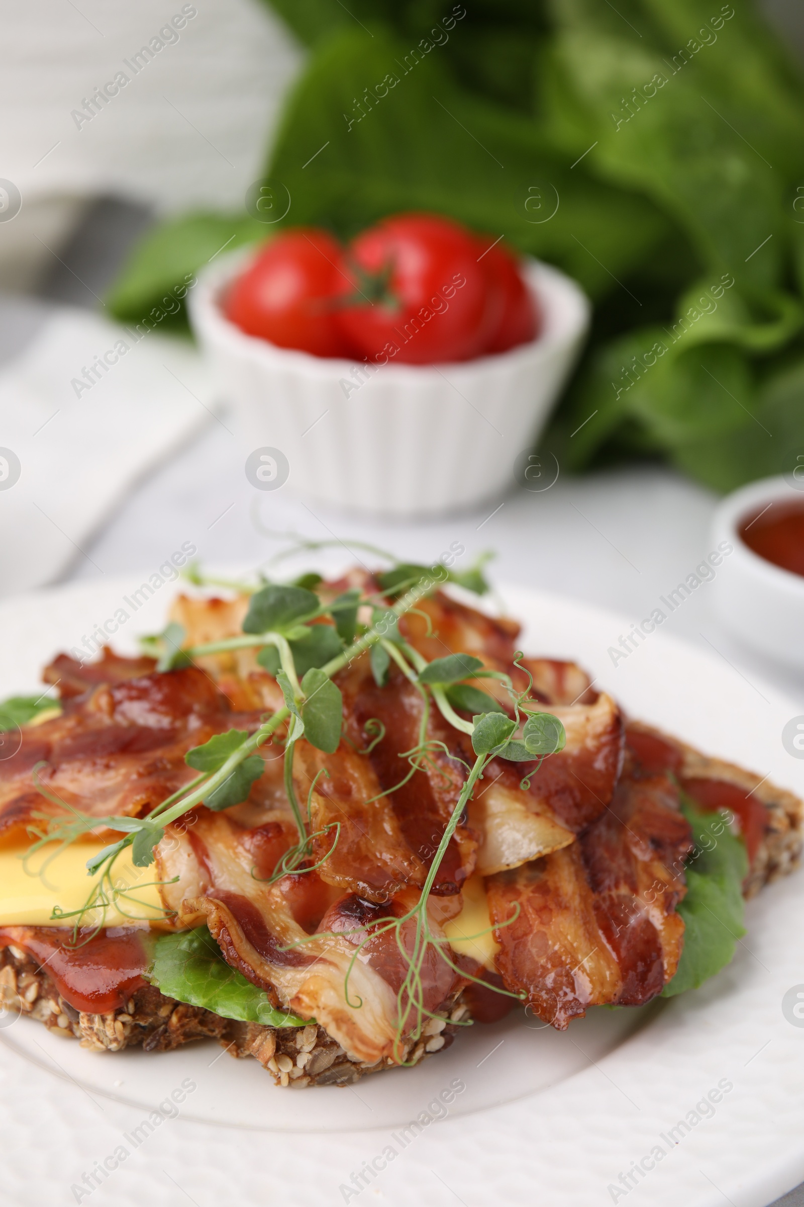 Photo of Tasty sandwich with bacon and microgreens on white table, closeup