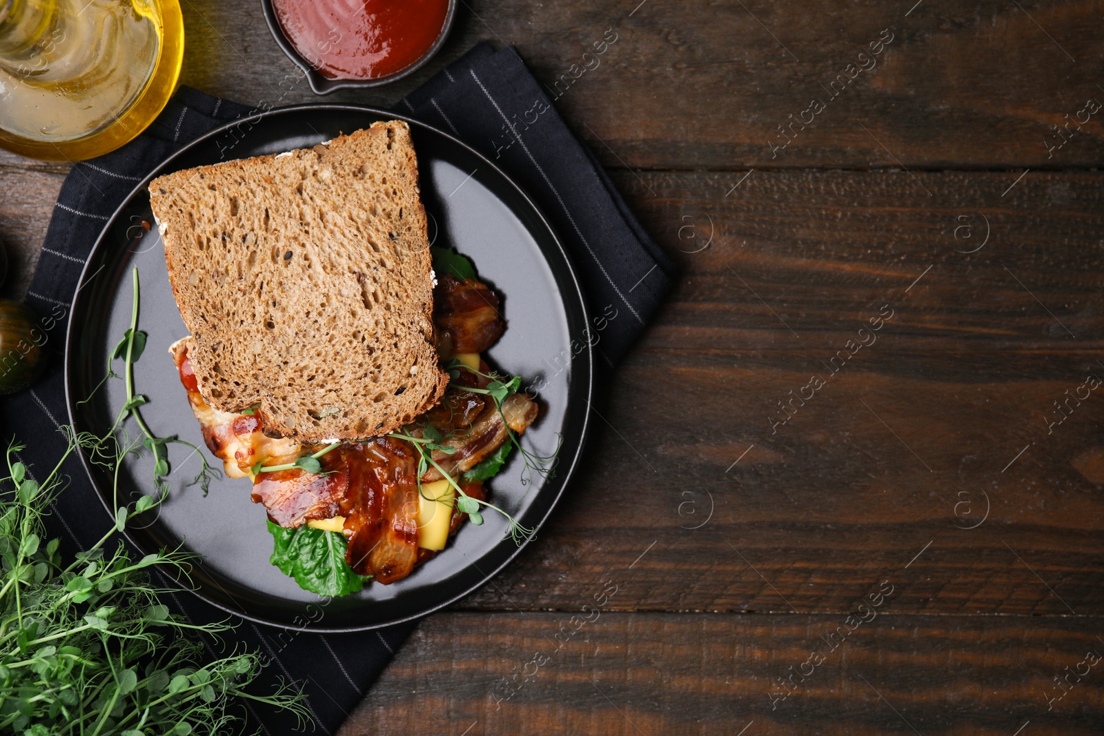 Photo of Tasty sandwich with bacon and microgreens served on wooden table, flat lay. Space for text