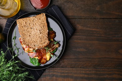 Photo of Tasty sandwich with bacon and microgreens served on wooden table, flat lay. Space for text