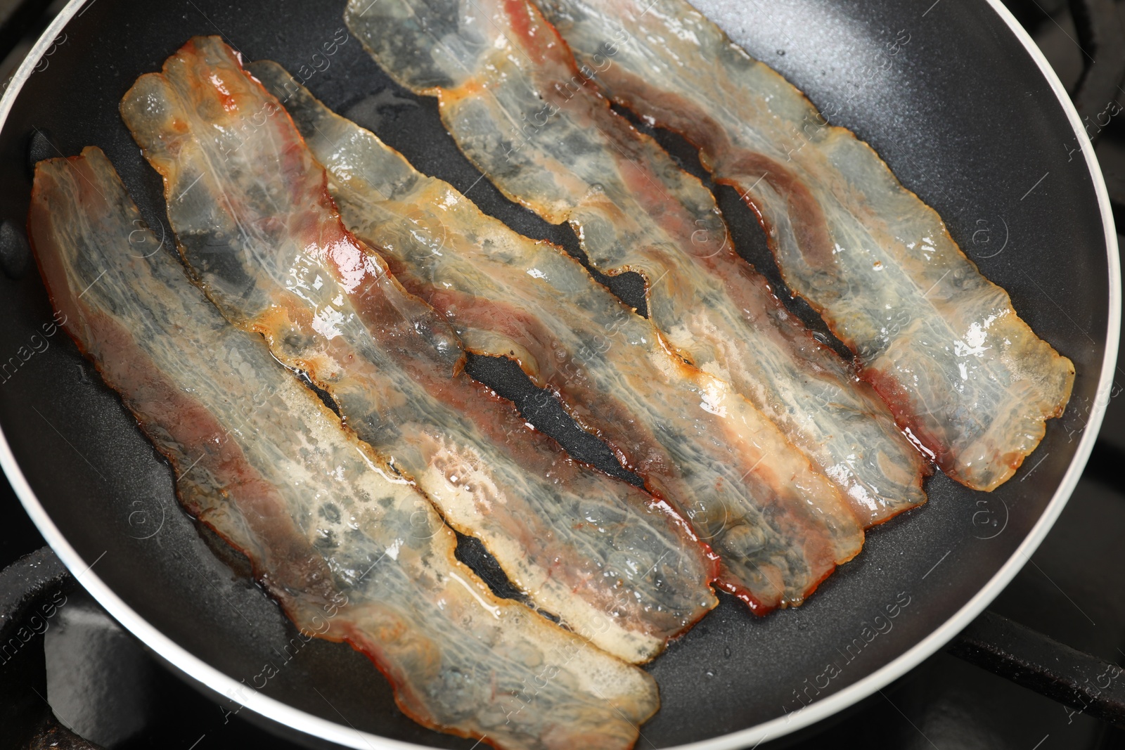 Photo of Slices of bacon frying in pan, closeup