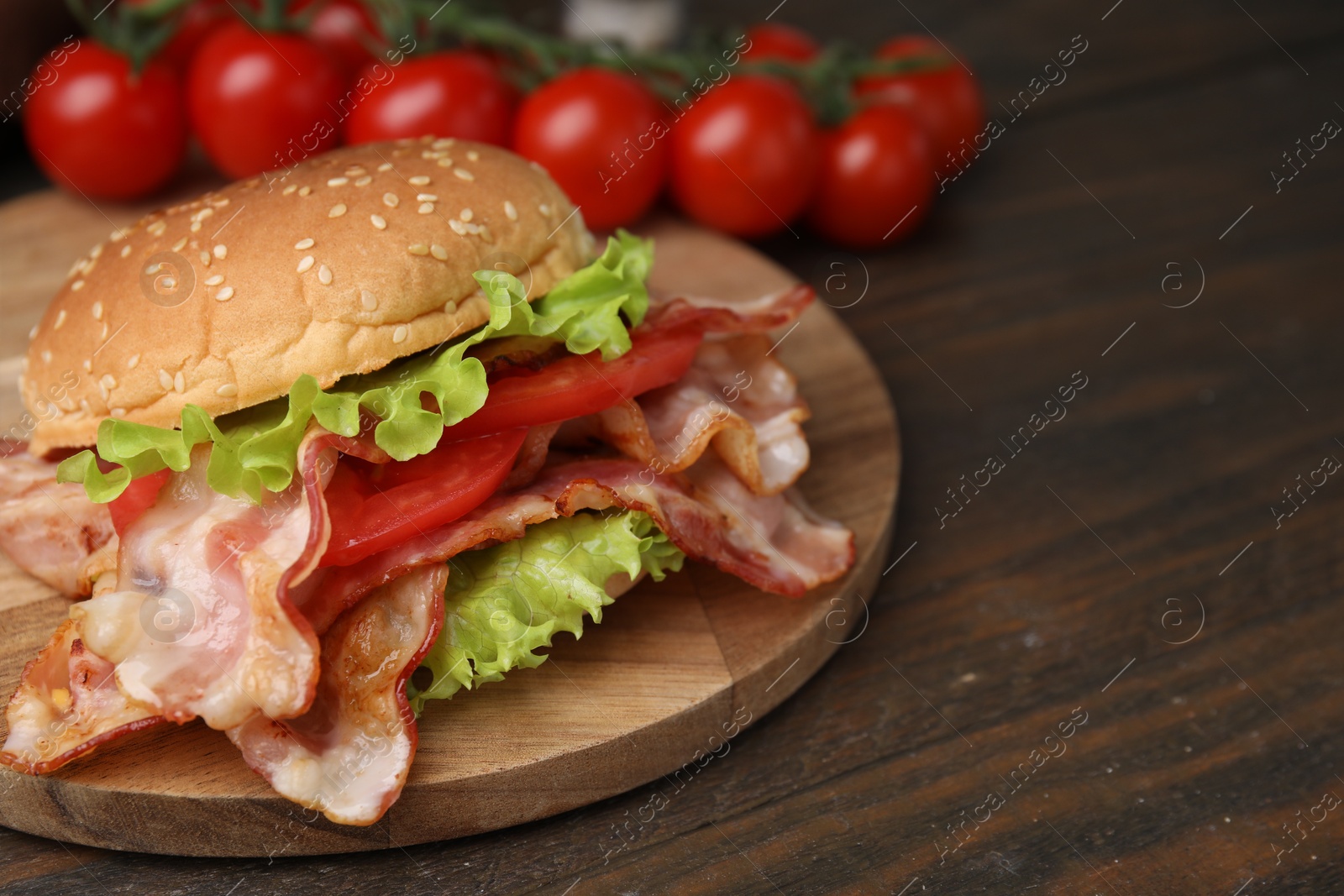 Photo of Delicious burger with bacon, tomato and lettuce on wooden table, space for text