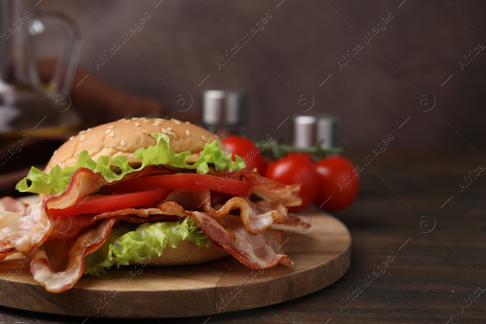 Photo of Delicious burger with bacon, tomato and lettuce on wooden table. Space for text