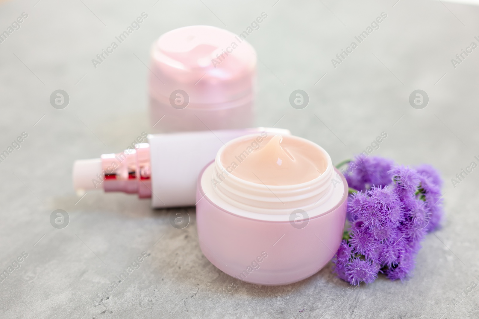 Photo of Set of different cosmetic products and ageratum flowers on gray table, closeup